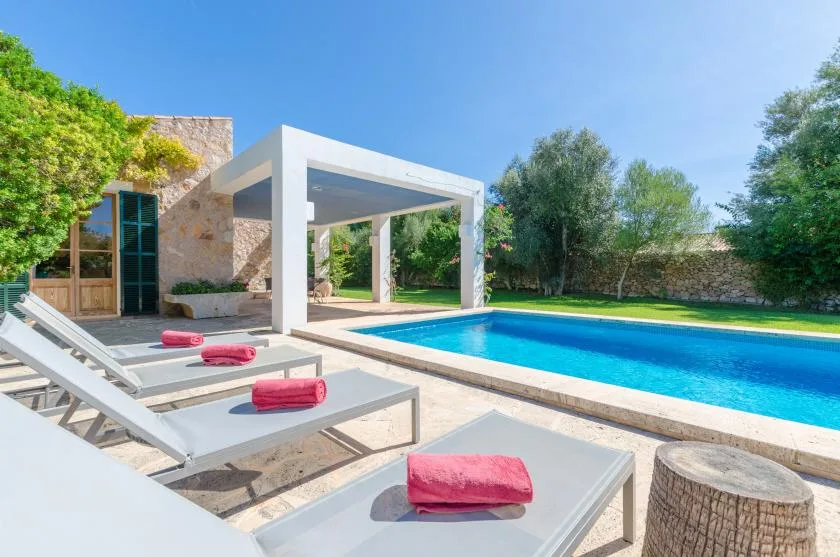 A swimming pool beside a modern patio with lounge seating and greenery.