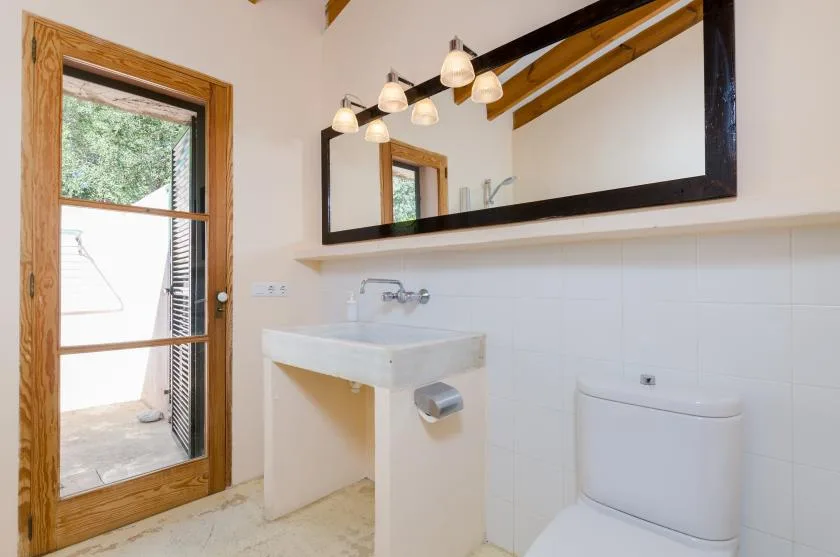 Un baño con lavabo de pared, inodoro y un espejo grande.