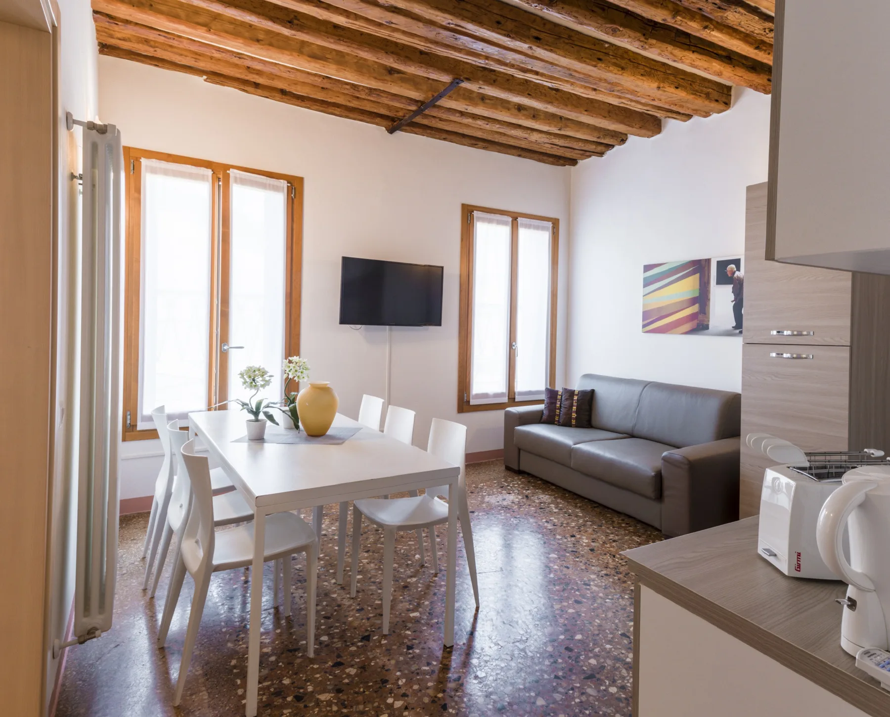 A bright living and dining area with a table, seating, and a wall-mounted television.