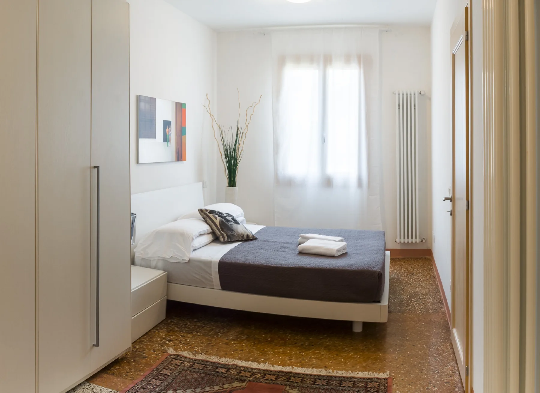 A bright bedroom with a bed and a window with sheer curtains.