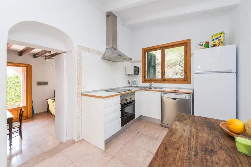A bright kitchen with white cabinets, a wooden table, and a window.