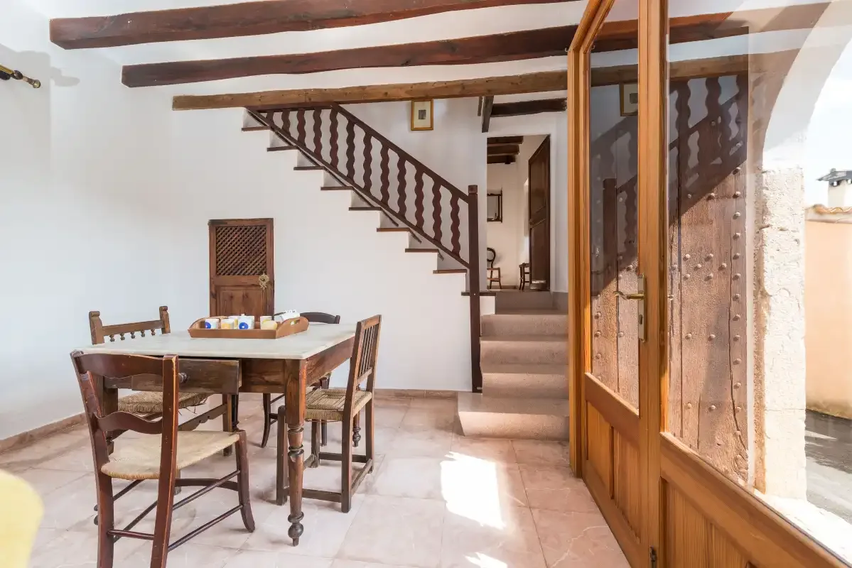 A bright dining area with a wooden table beside a staircase and glass doors.