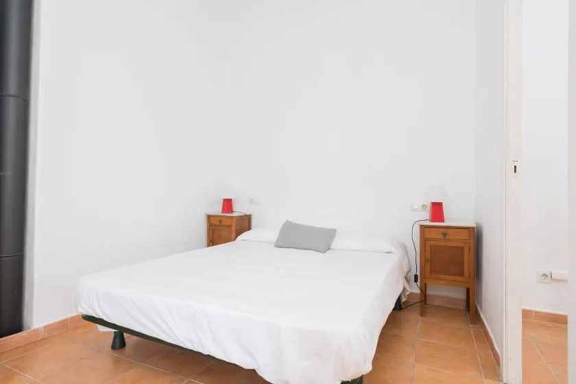 A bedroom with a white bed, wooden bedside tables, and red lamps.
