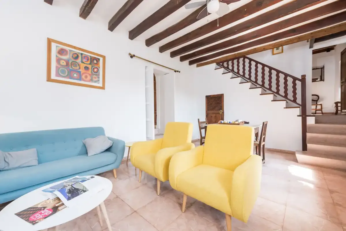 A living room with blue and yellow seating, a coffee table, and a staircase.