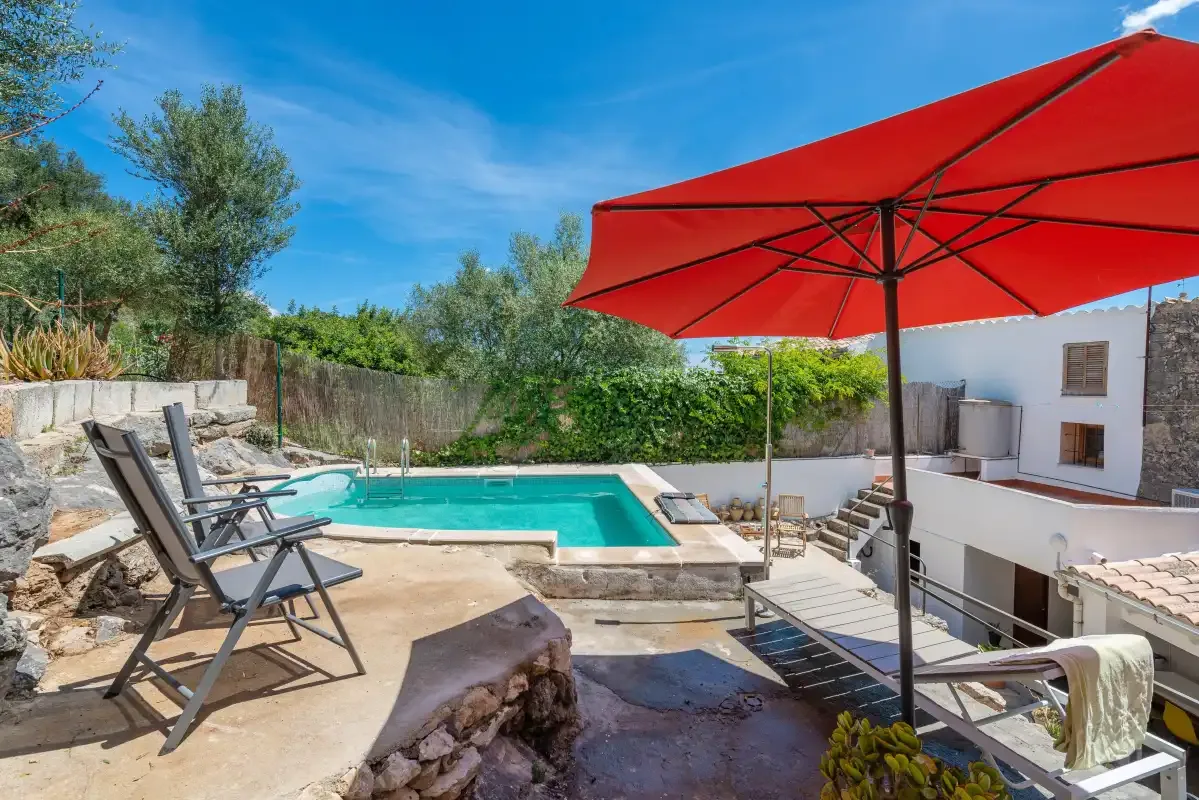 A swimming pool and outdoor seating area sit beneath a large red umbrella.