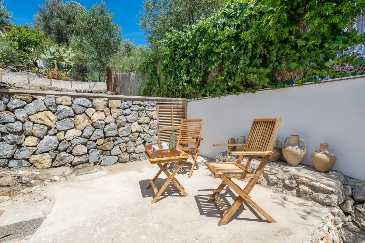 A stone patio with wooden seating beside a white garden wall.
