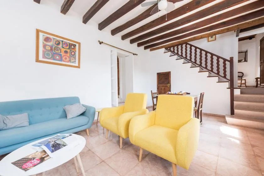 A bright living room with colorful seating beneath exposed ceiling beams.
