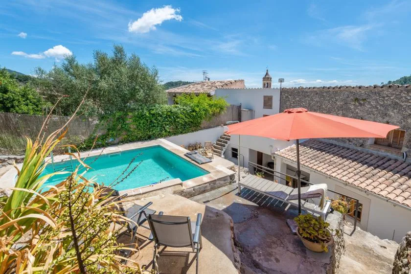An outdoor swimming pool and patio seating beneath a large umbrella.