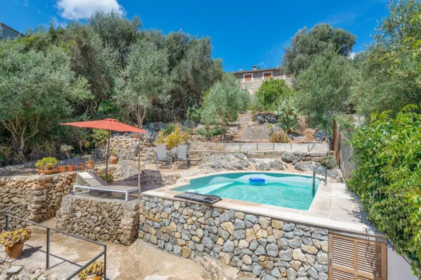 An outdoor swimming pool sits among stone terraces and leafy trees.