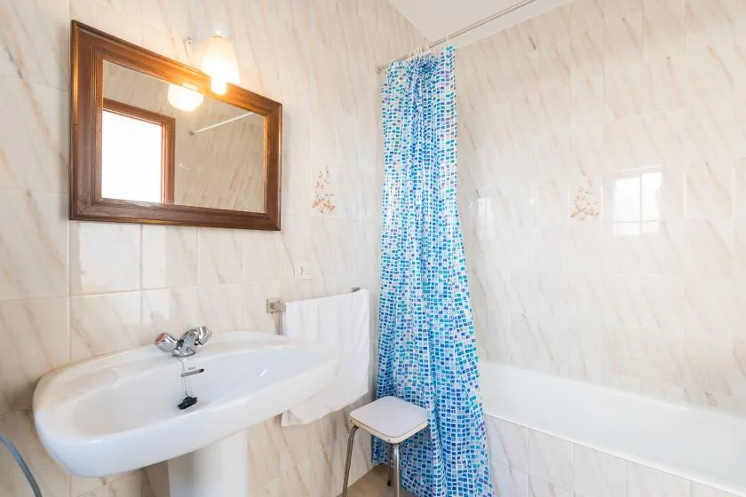 A tiled bathroom with a sink, bathtub, and blue patterned shower curtain.