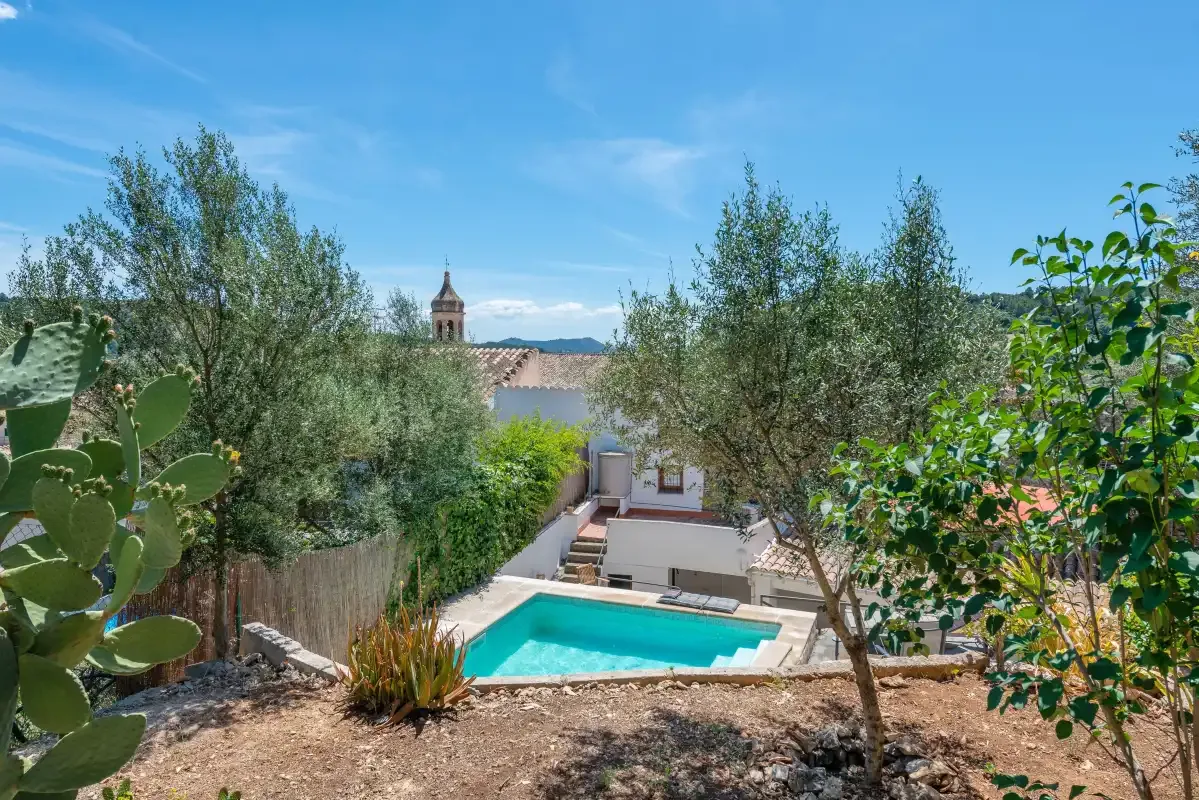 A garden courtyard with a swimming pool, trees, and a distant church tower.