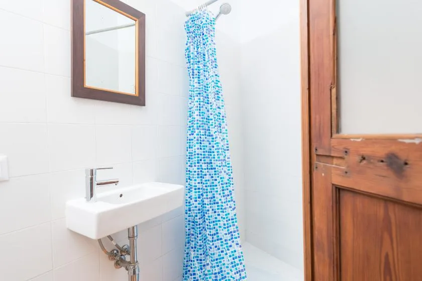 A tiled bathroom with a wall-mounted sink and blue patterned shower curtain.