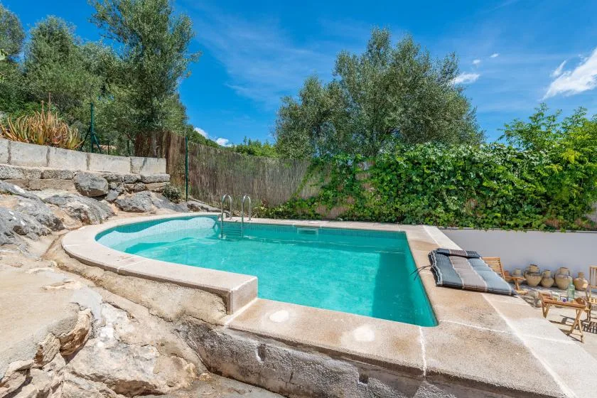 An outdoor swimming pool sits beside a rocky garden, with lounge seating nearby.