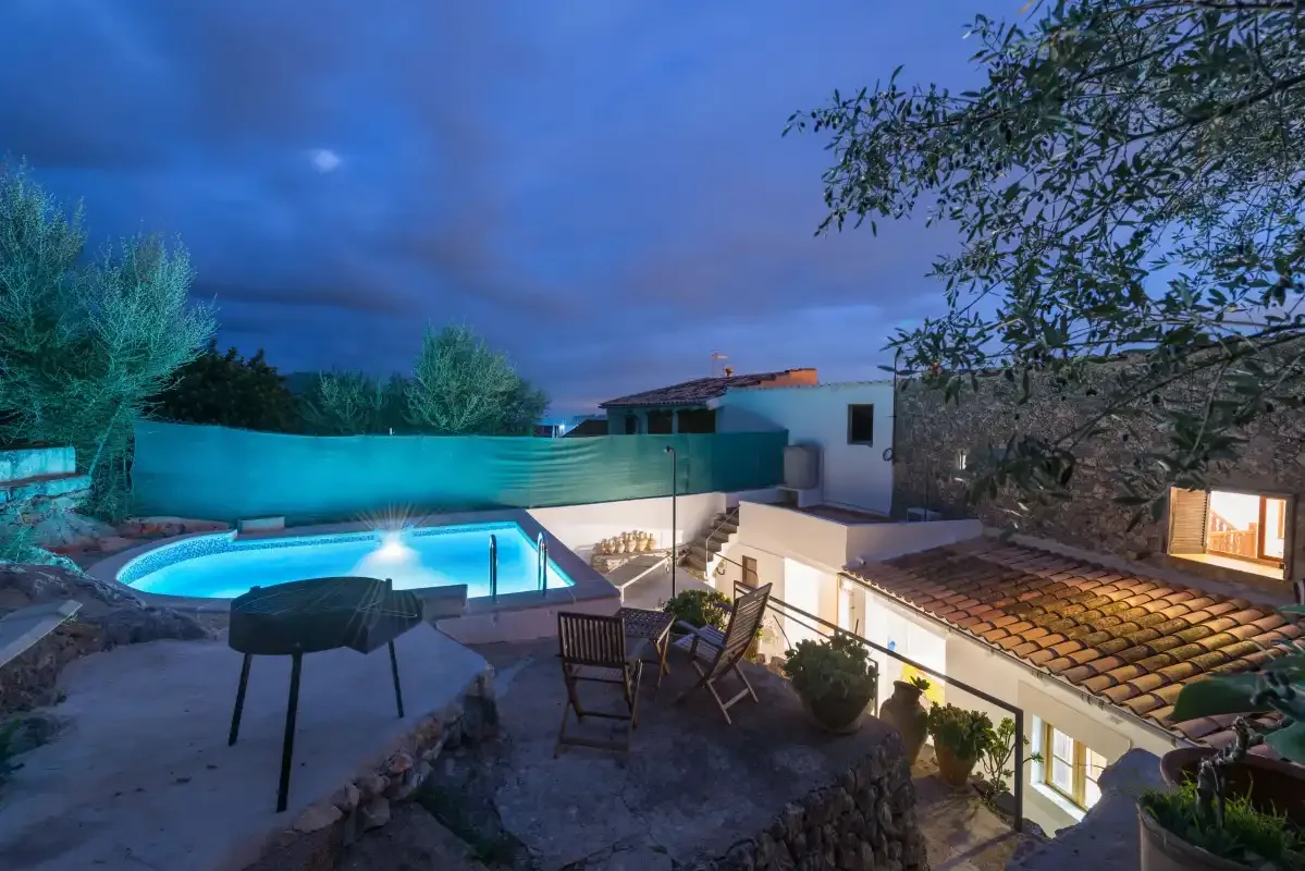A poolside terrace with outdoor seating overlooks a lit swimming pool at dusk.