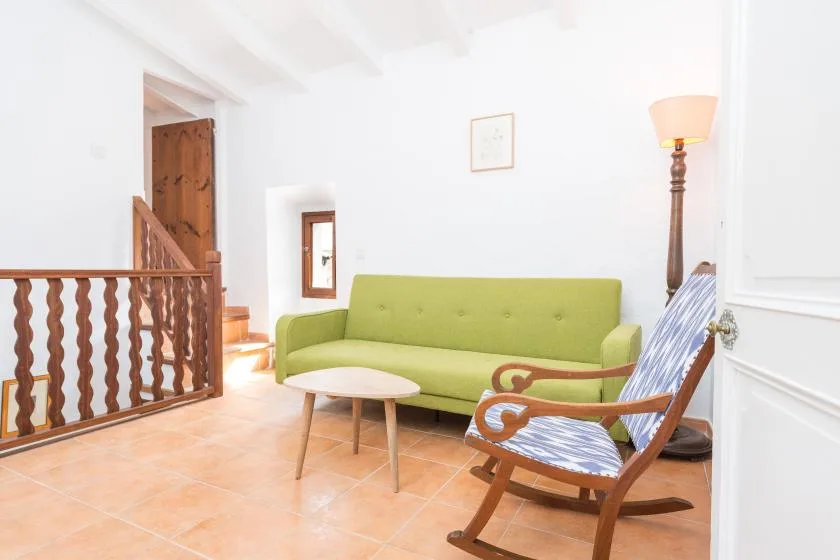A bright sitting room with green seating, a wooden chair, and a small table.