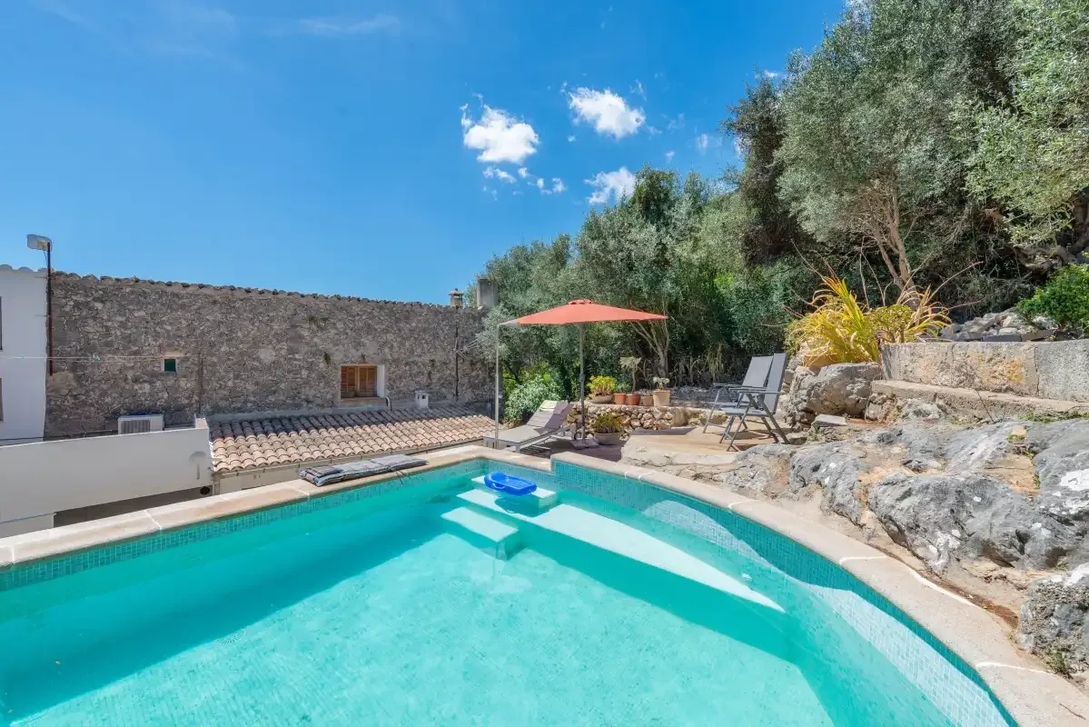 An outdoor swimming pool beside a stone wall, with loungers and trees nearby.