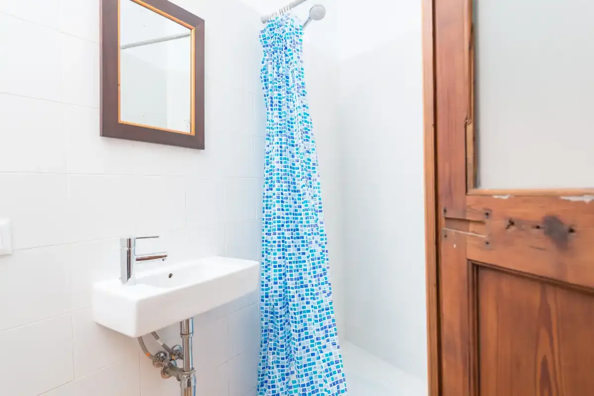 A bright bathroom with a wall-mounted sink and blue patterned shower curtain.
