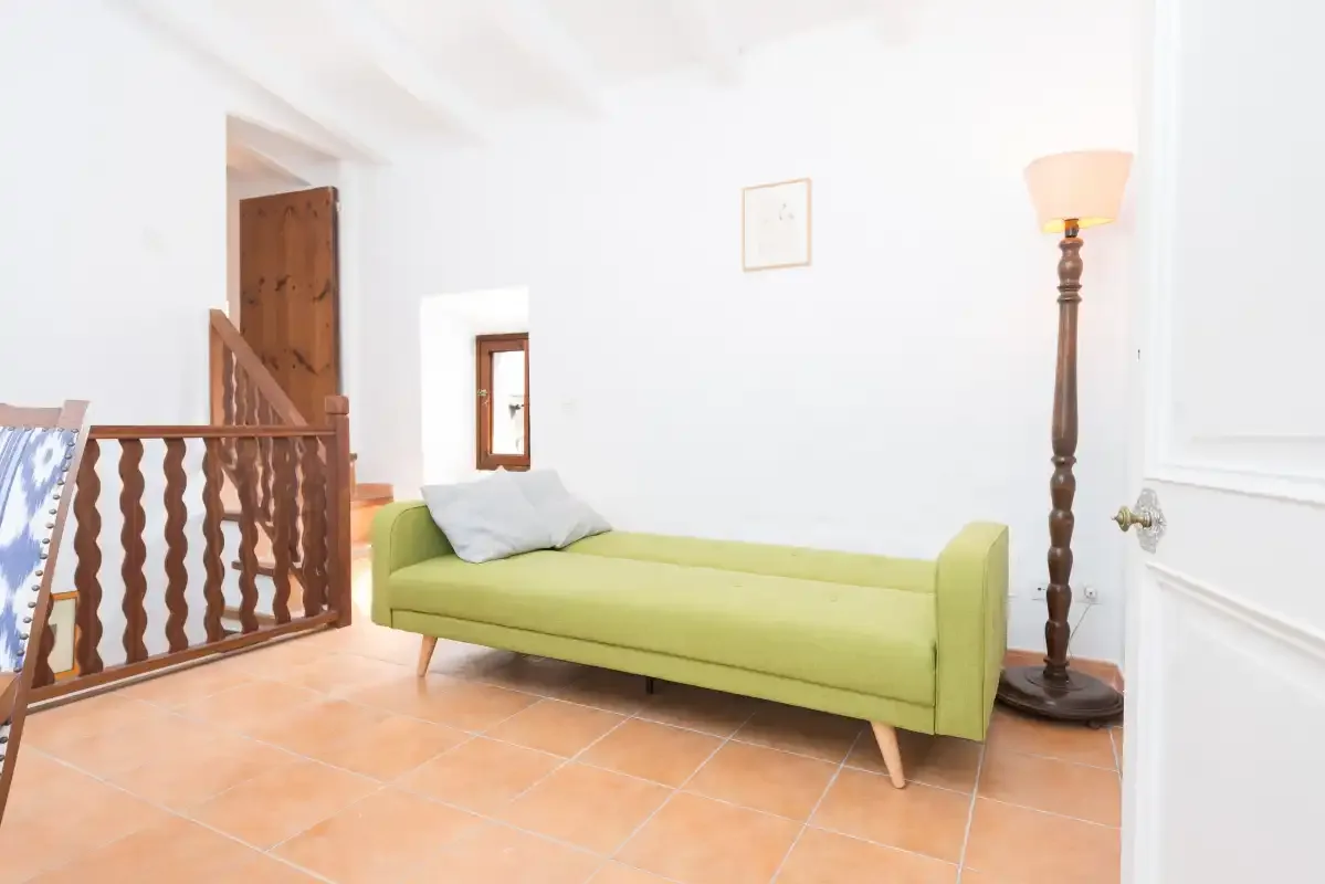 A bright sitting area with a green upholstered daybed and tiled floor.