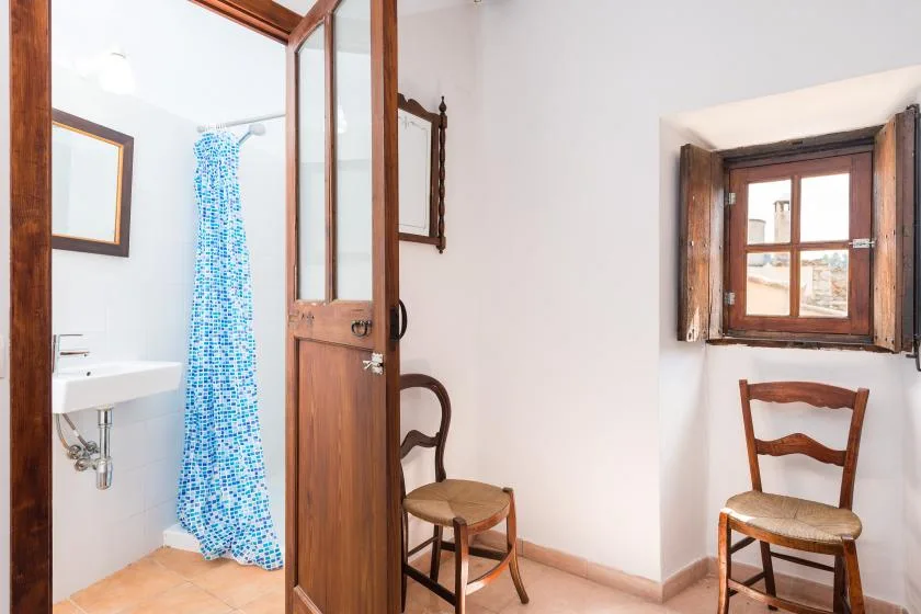 A bright room with a sink, a blue shower curtain, and wooden chairs.