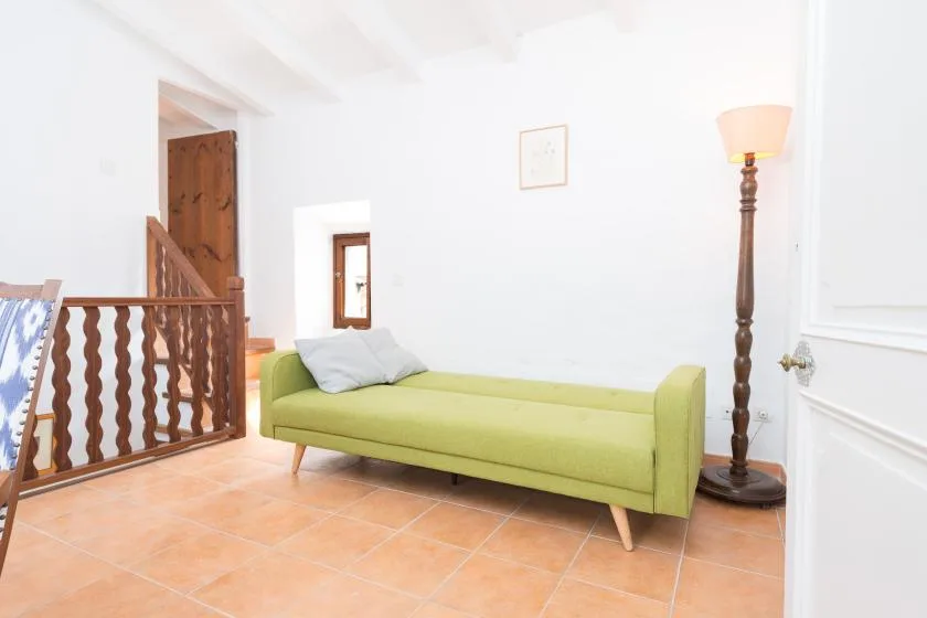 A bright living area with a green sofa, floor lamp, and tiled floor.