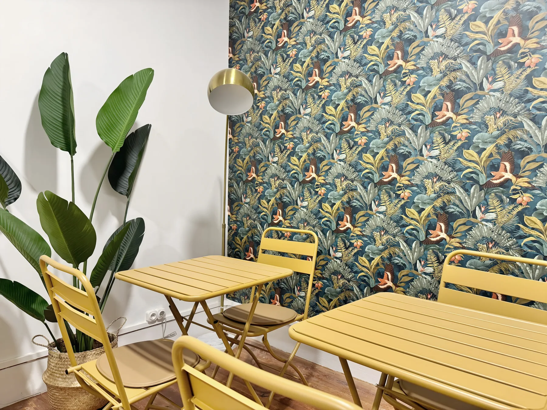 A dining area with yellow tables and chairs beside a leafy patterned wall.