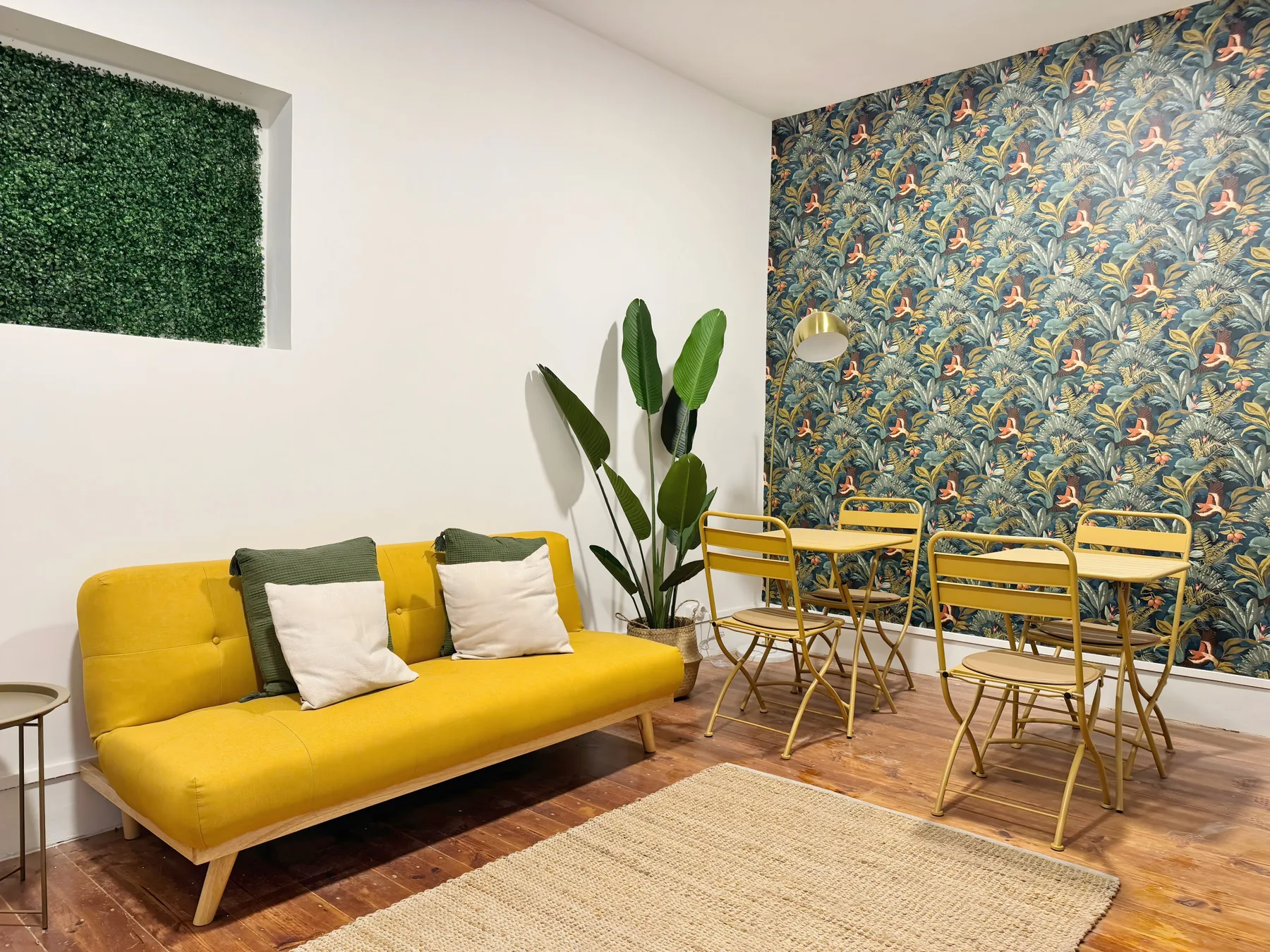 Living and dining area with yellow seating, a table, and patterned wallpaper.