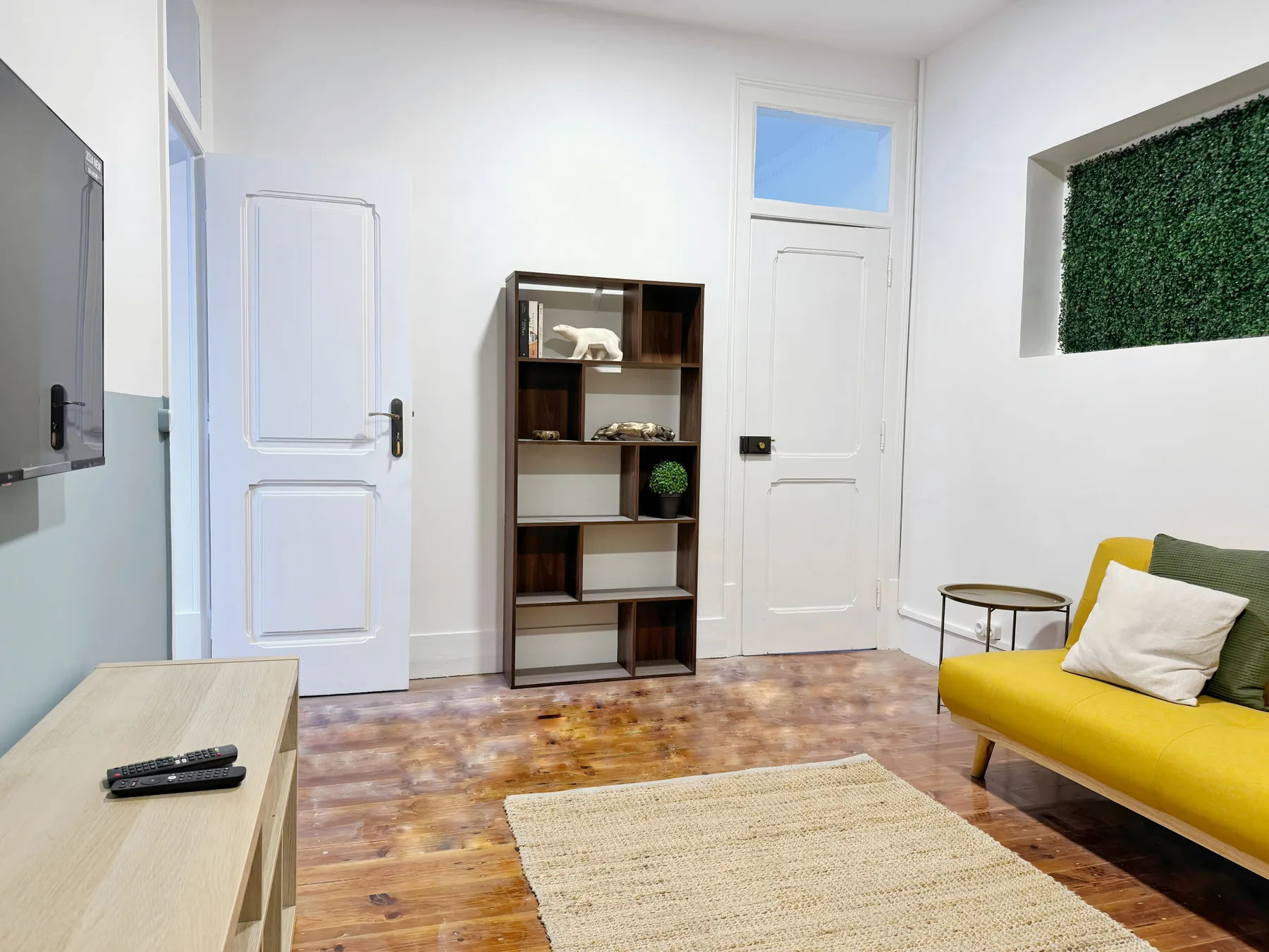 A bright living room with yellow seating, a wooden shelf, and a pale rug.
