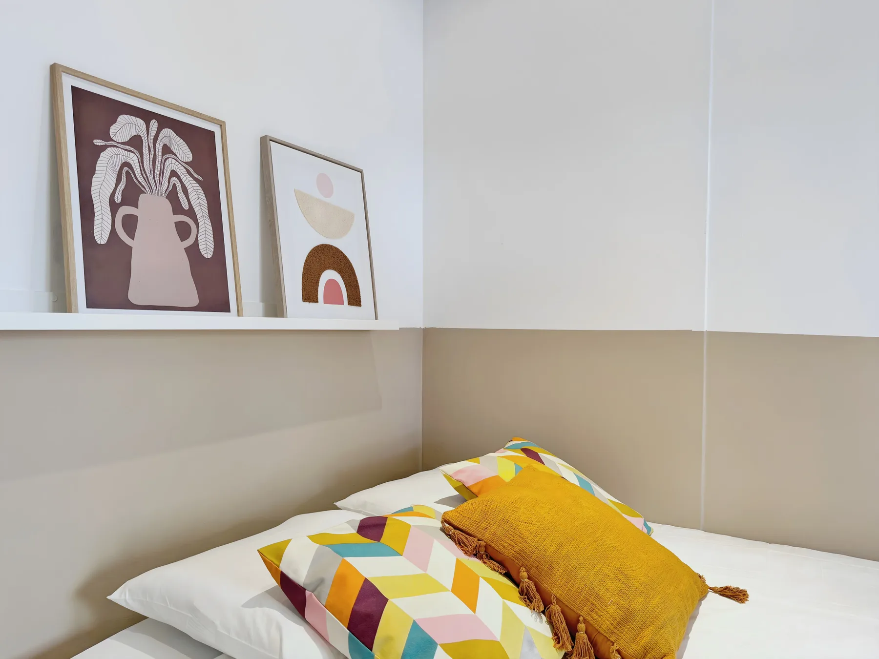 A bedroom with a bed and colorful pillows beneath framed artwork.
