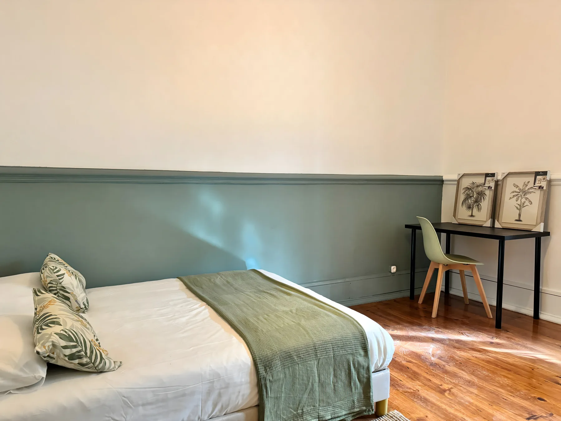 A bedroom with a bed, green wall paneling, and a small desk.