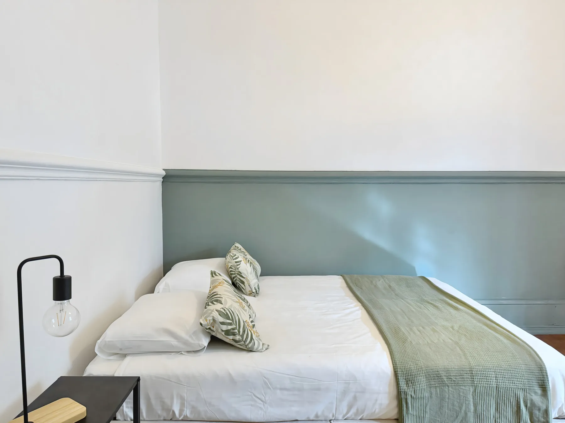 A bedroom with a neatly made bed and a green throw.