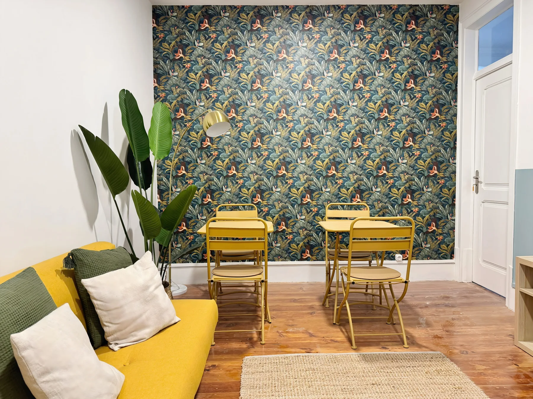 A living area with yellow seating and a small dining table against a patterned wall.
