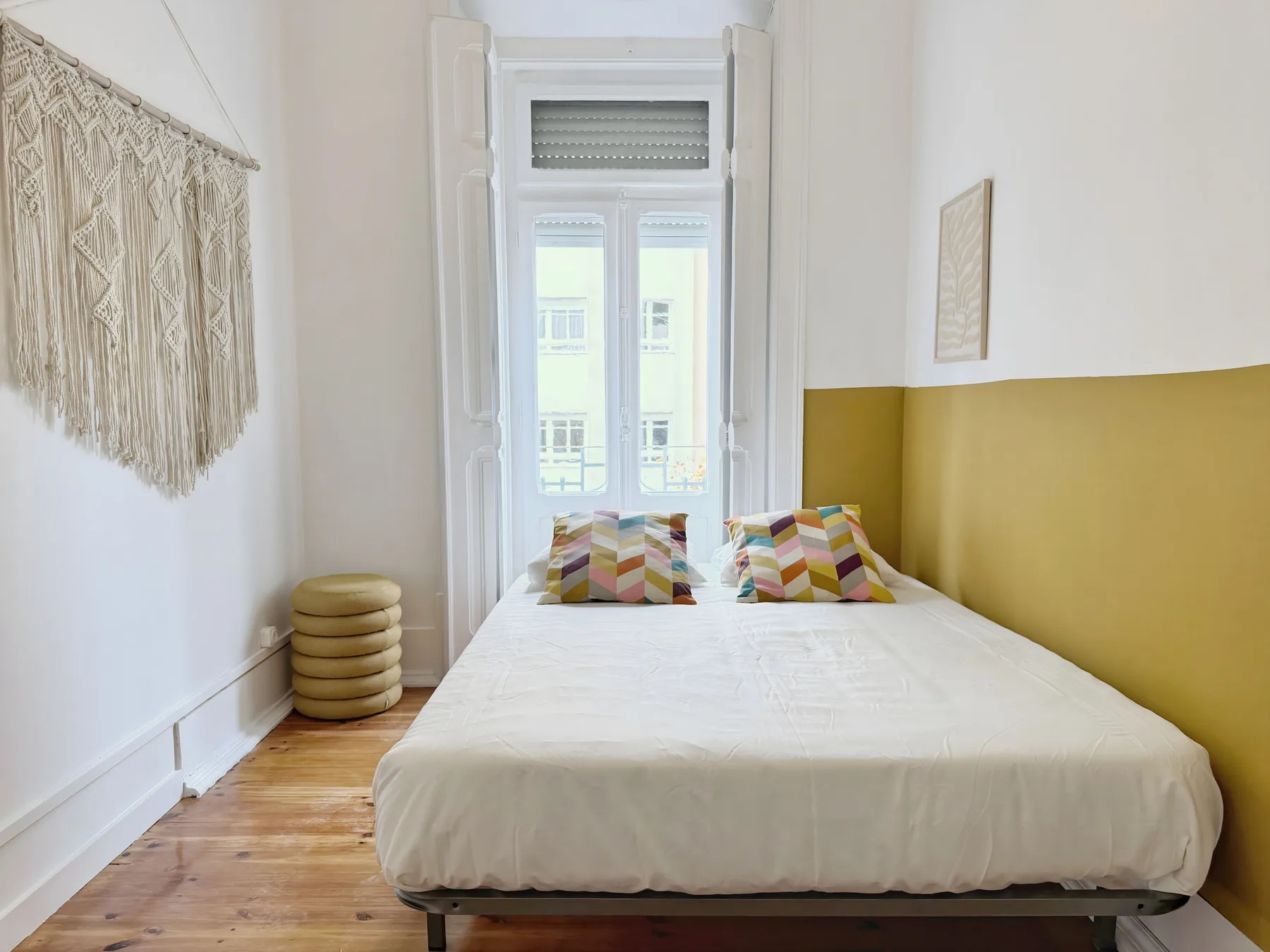 A bedroom with a bed beneath a tall window and colorful pillows.