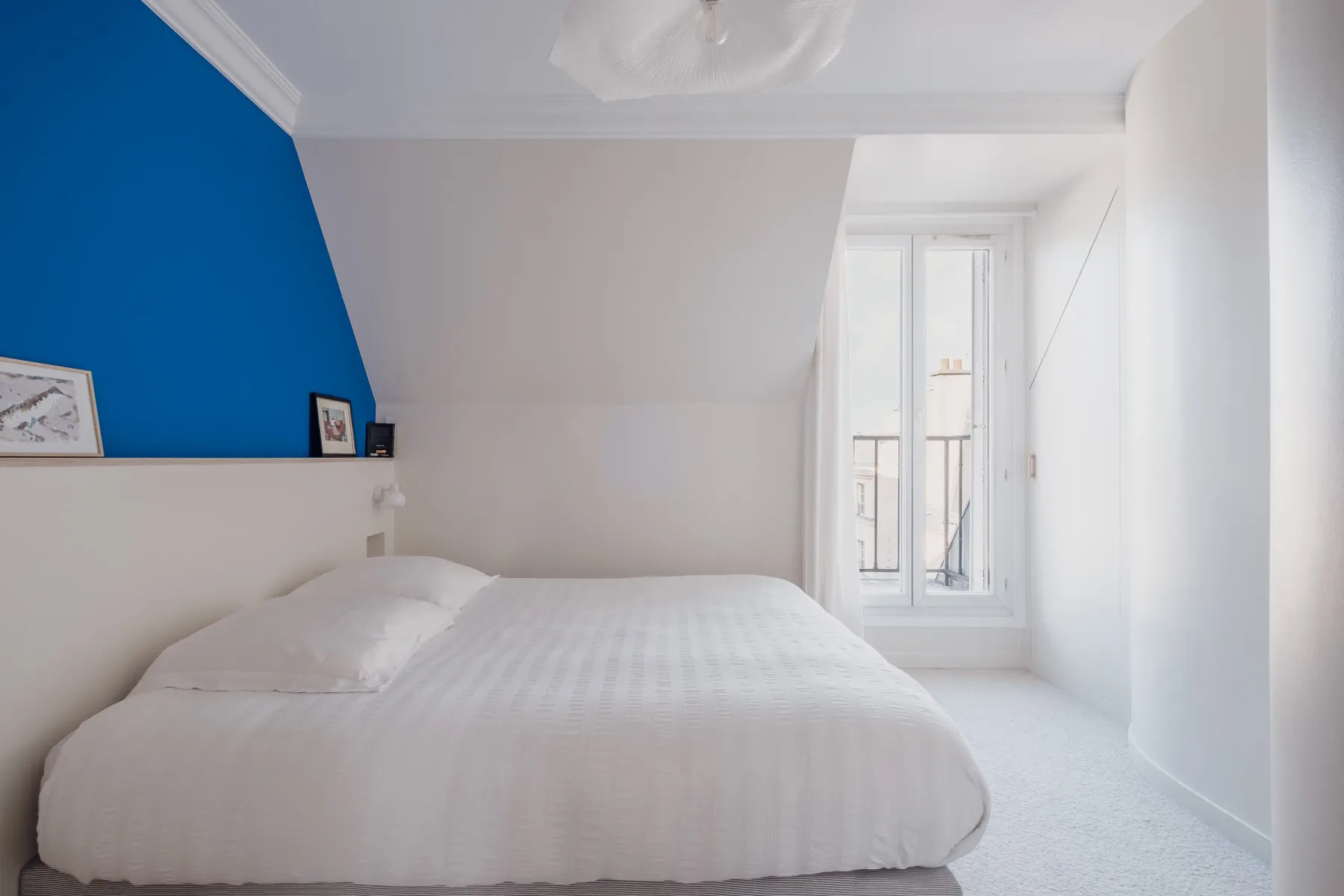A bright bedroom with a bed beneath a sloped ceiling.