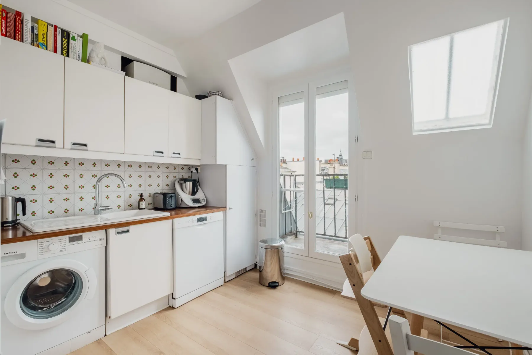 A bright kitchen with white cabinets, appliances, and a dining table by the window.