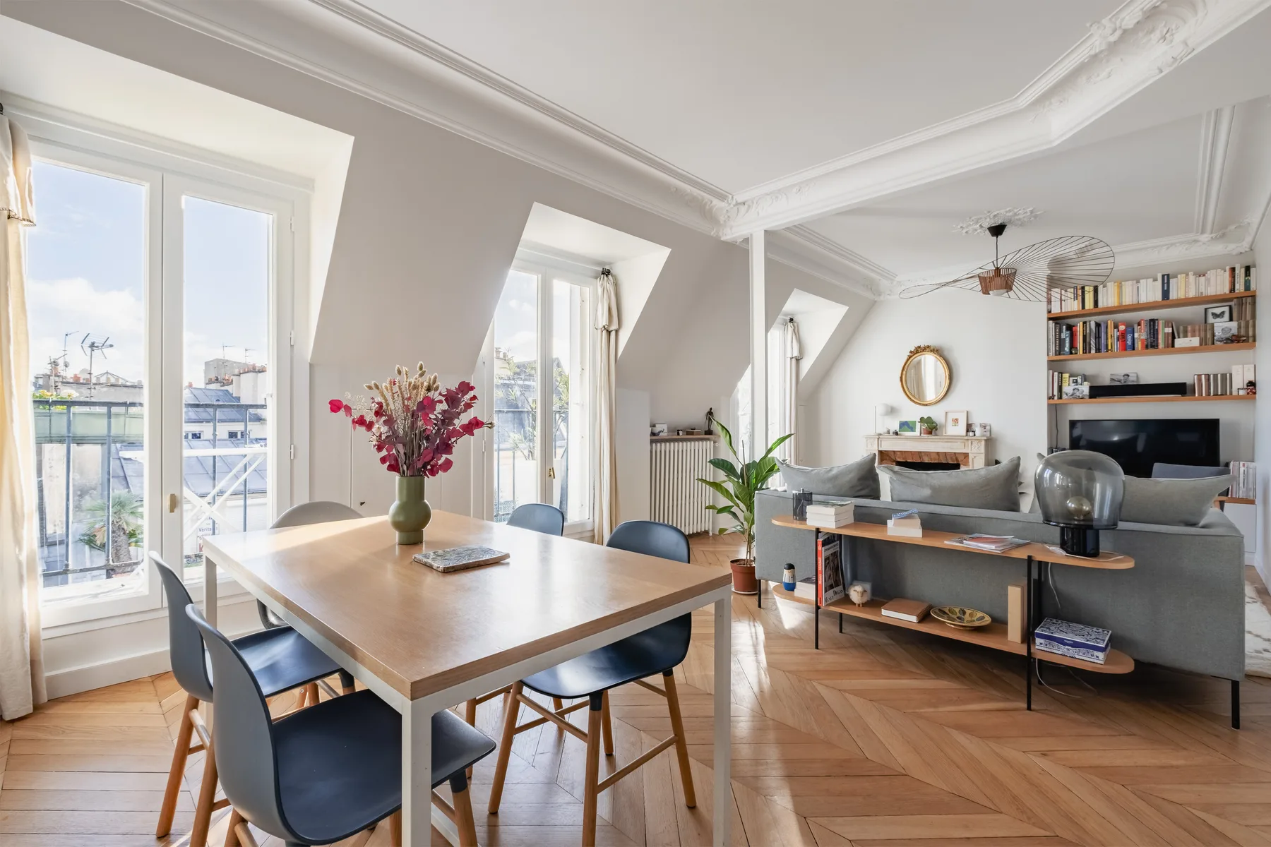 A bright living and dining area with a wooden table and seating beside tall windows.