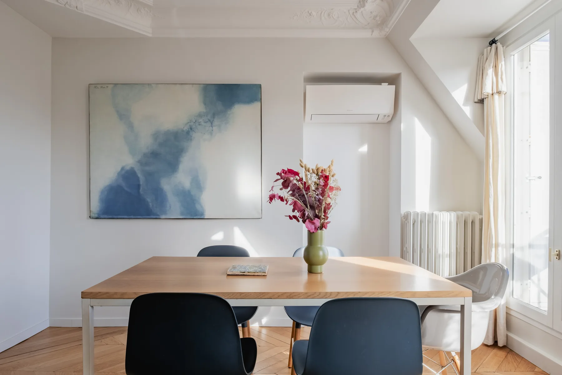 A bright dining area with a wooden table, dark seating, and a vase of flowers.