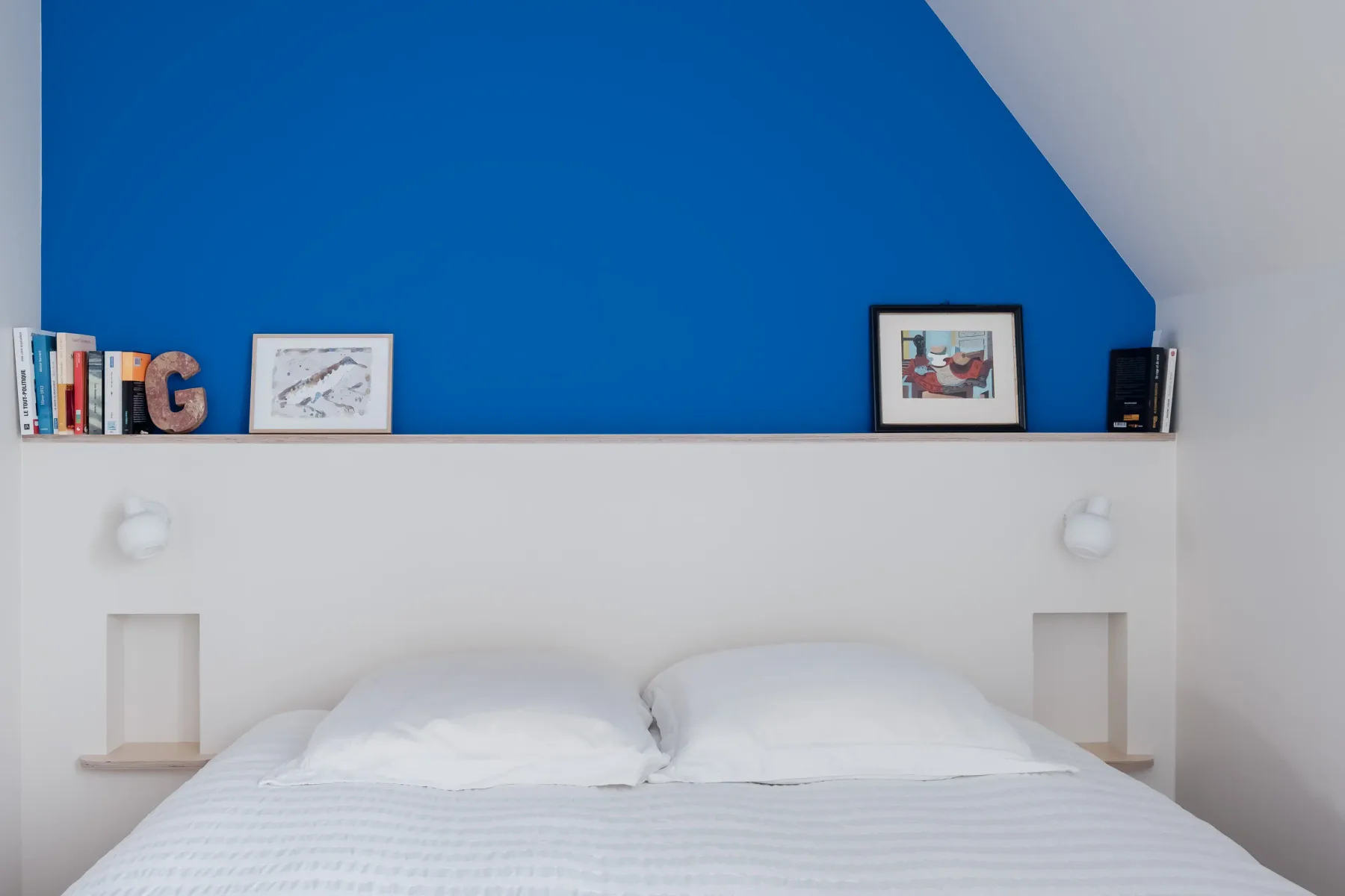 A bedroom with a neatly made bed beneath a vivid blue accent wall.