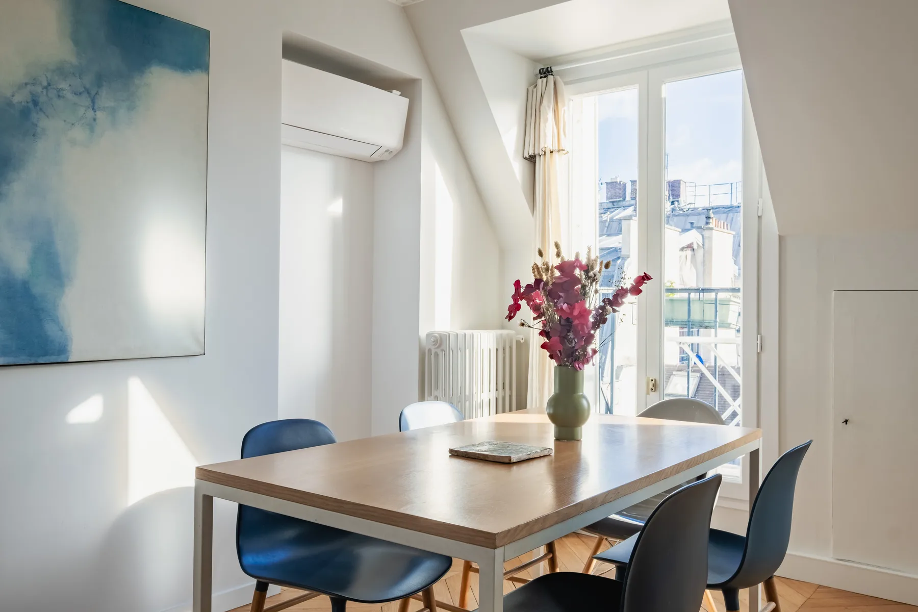 A bright dining area with a wooden table beside tall windows.