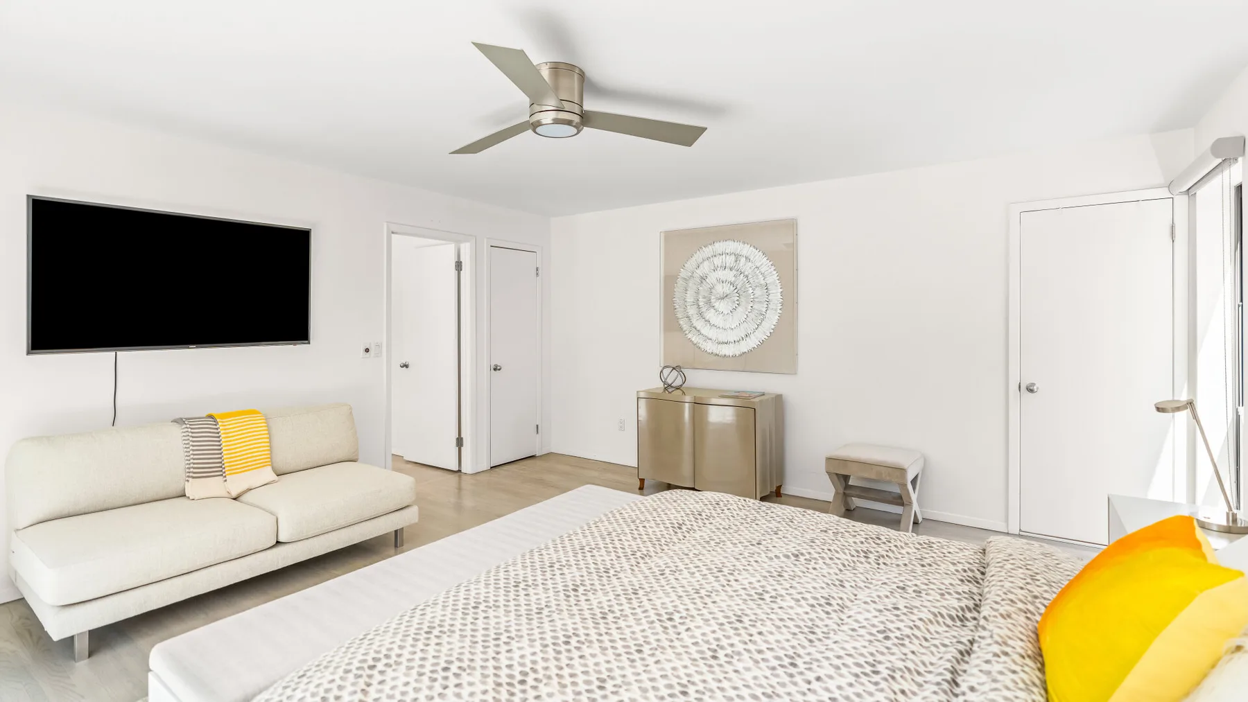 Una sala luminosa con sofá, televisor montado en la pared y alfombra estampada.