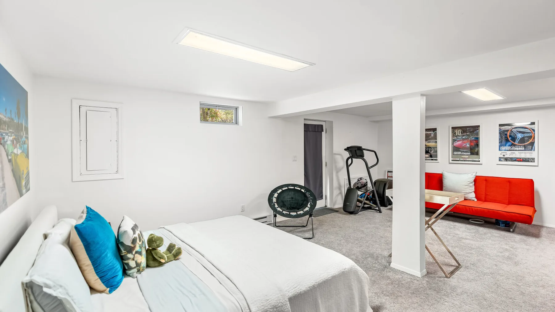 Una luminosa habitación en el sótano tiene una cama, equipo de ejercicio y un sofá rojo.