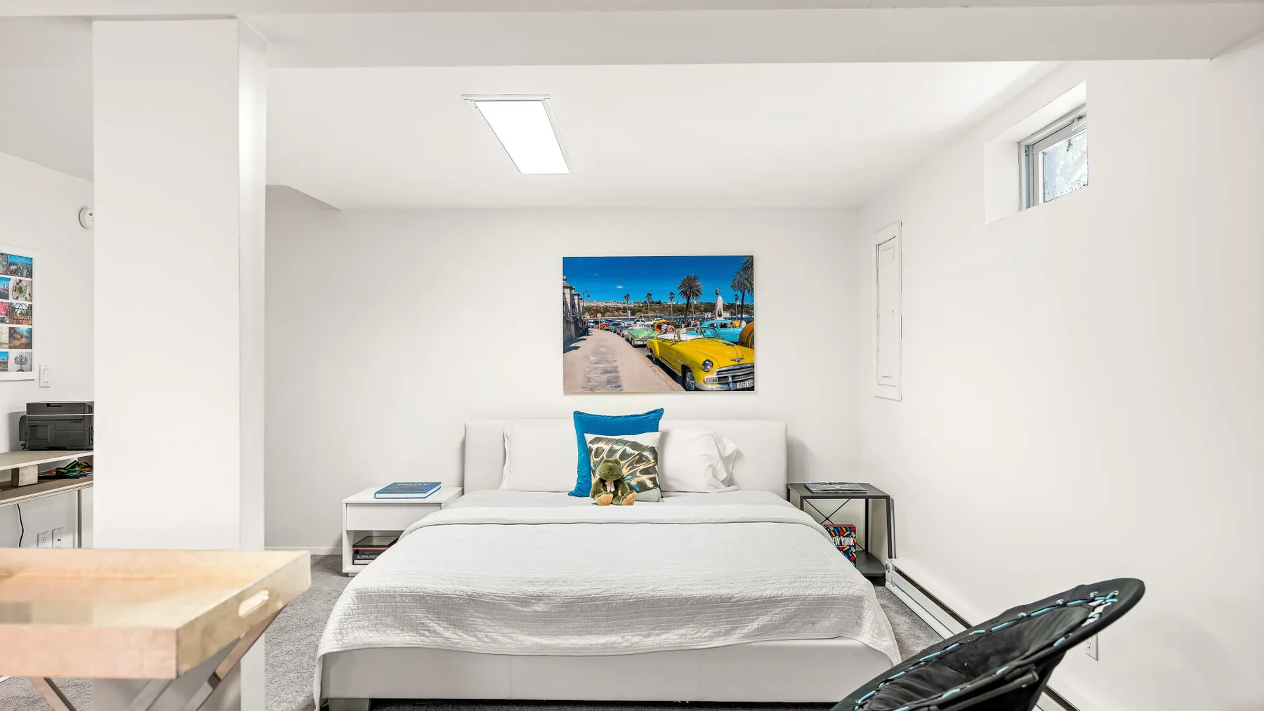 Un dormitorio luminoso tiene una cama bien hecha bajo un cuadro colorido.