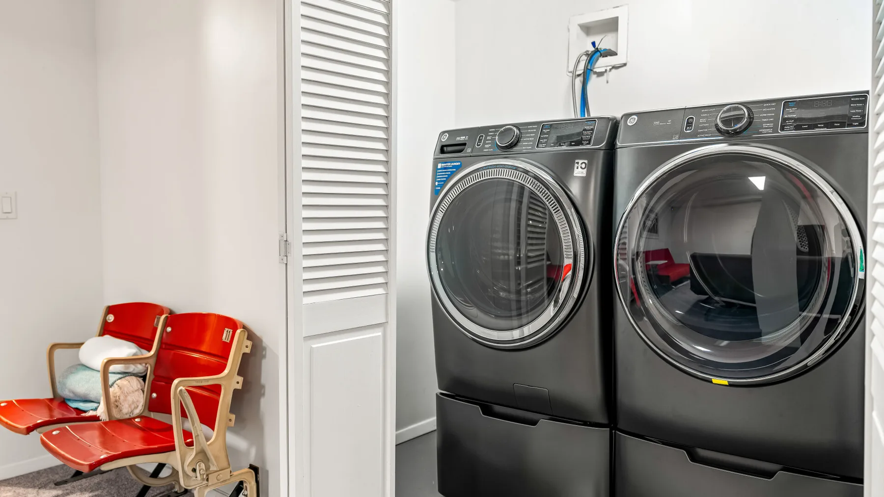 Un cuarto de lavandería con una lavadora y una secadora junto a asientos rojos.