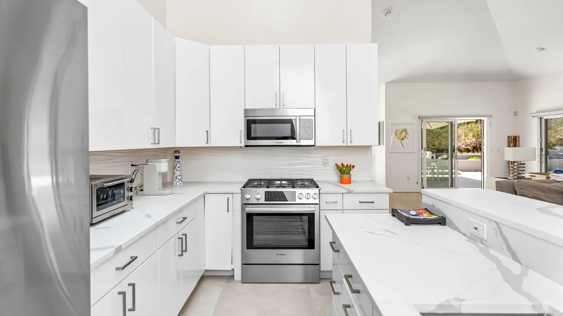 Una cocina blanca y luminosa con electrodomésticos de acero inoxidable y una isla larga.