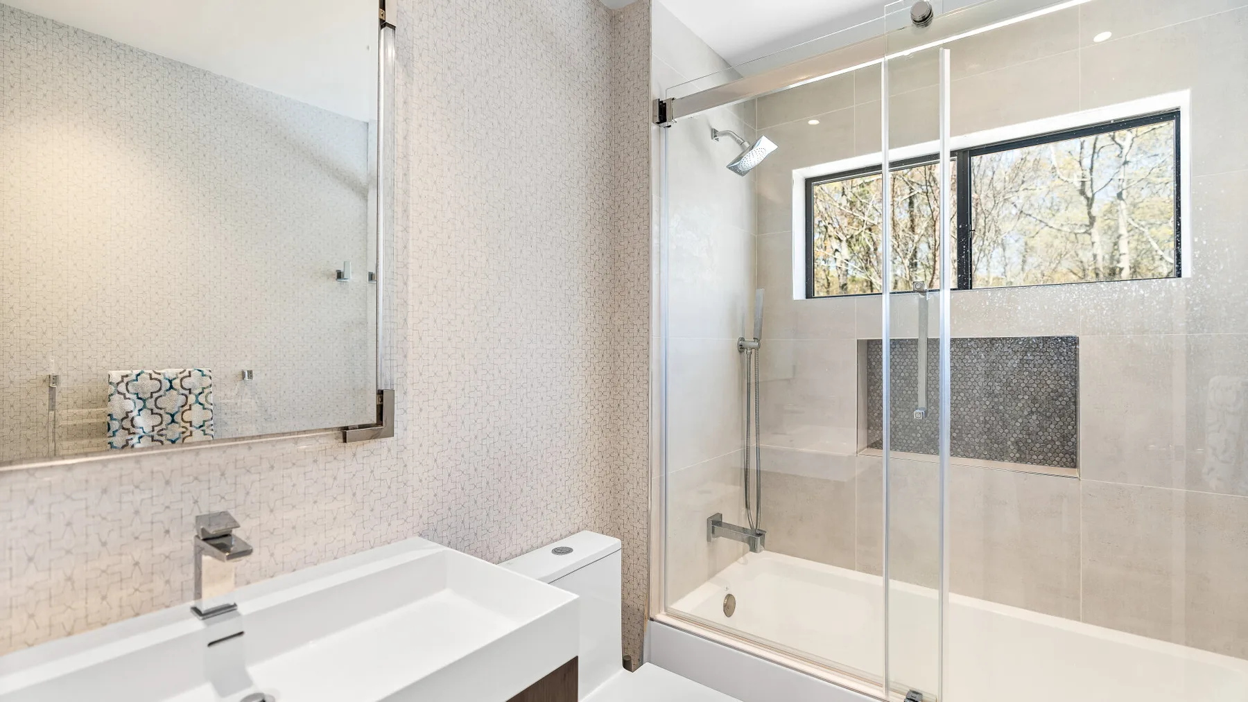 Baño luminoso con ducha de vidrio y una ventana amplia.