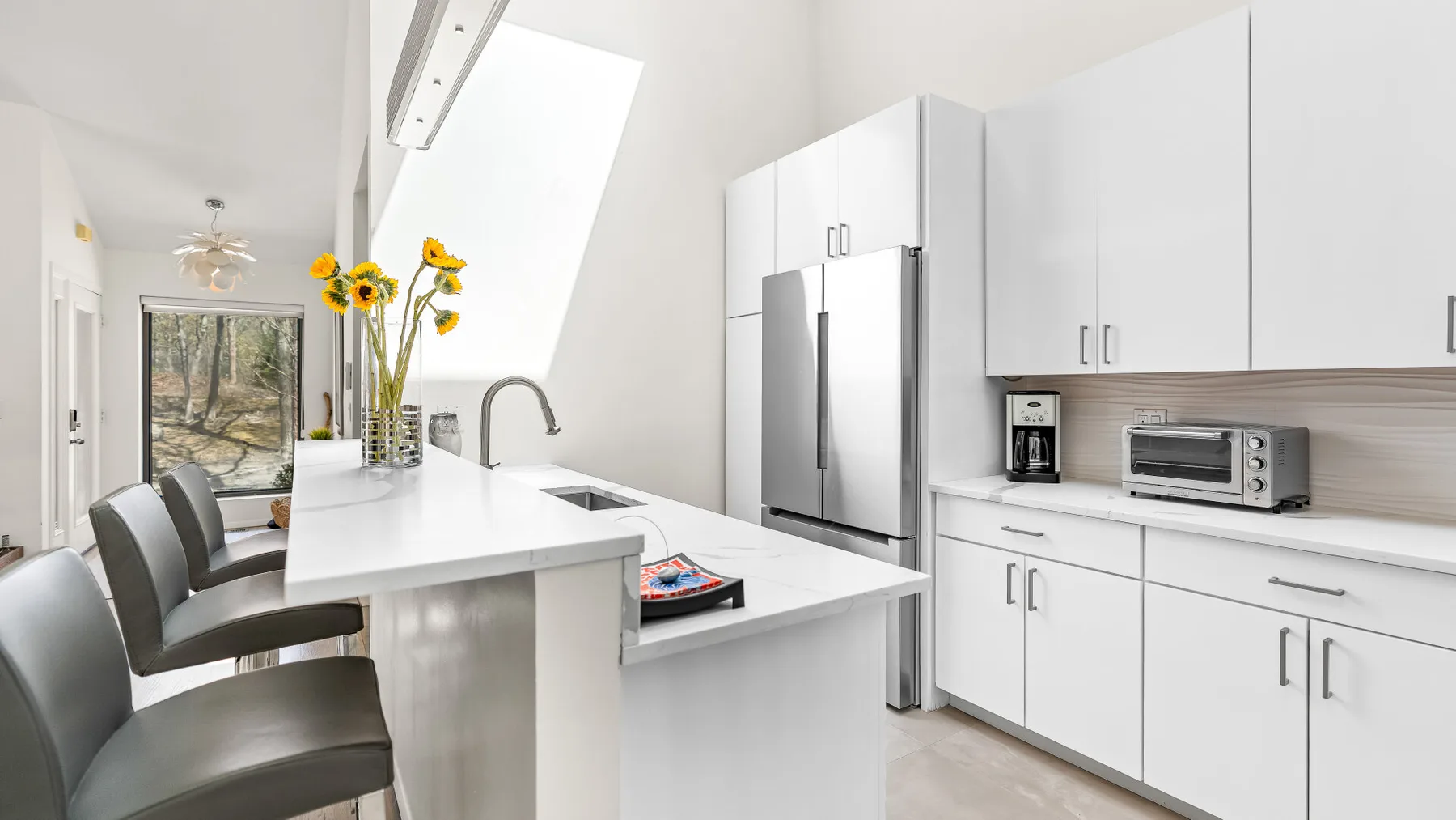 Una cocina moderna y luminosa con gabinetes blancos, electrodomésticos de acero inoxidable y una encimera.