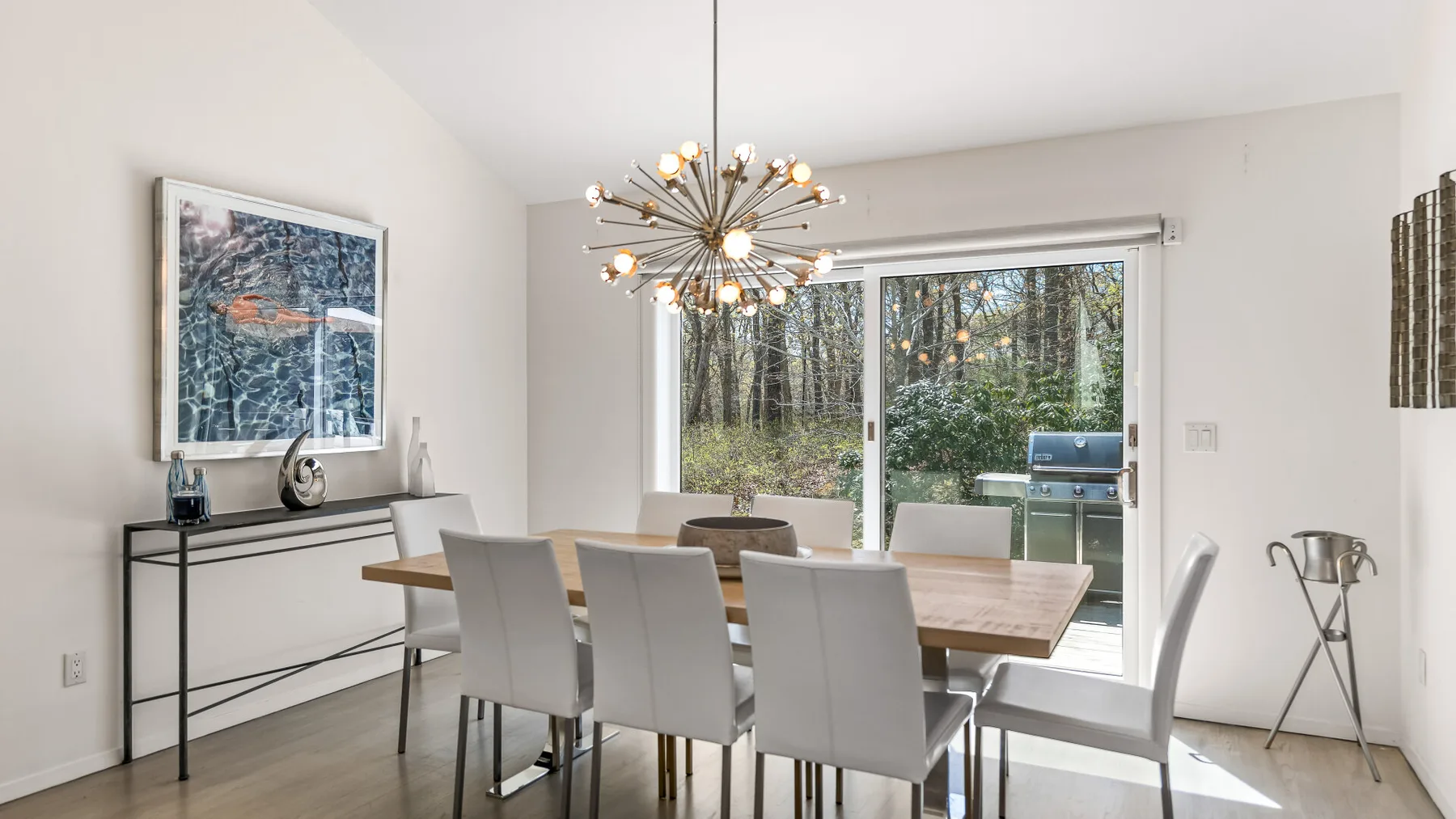 Un comedor luminoso con una mesa larga y grandes puertas de vidrio hacia la vegetación.