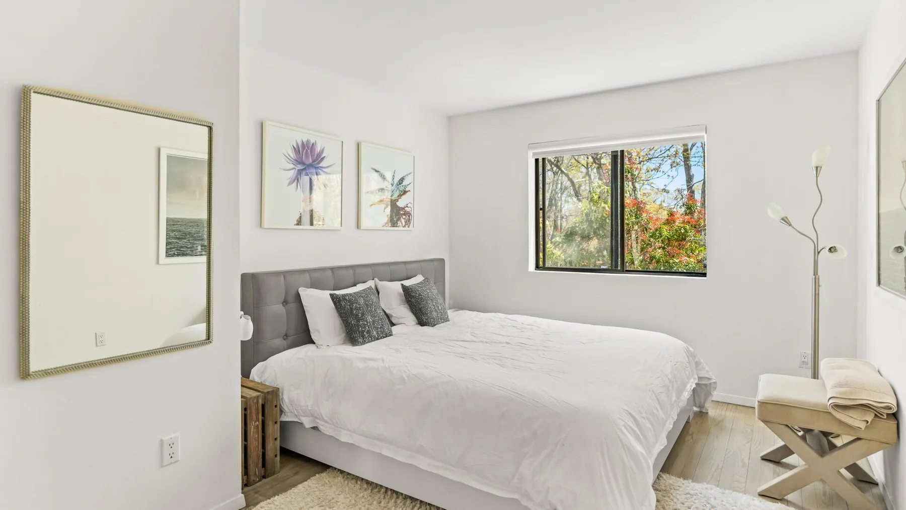 Un dormitorio luminoso con una cama, cuadros enmarcados y una ventana con árboles a la vista.