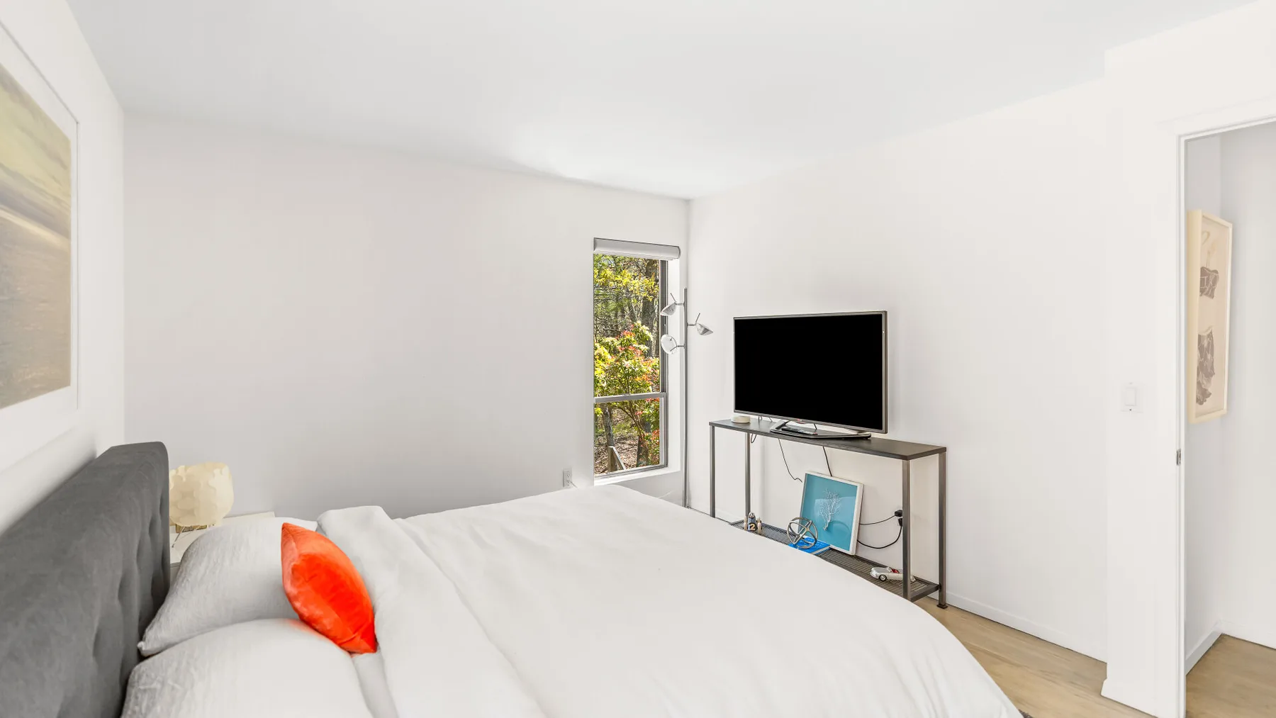 Un dormitorio luminoso con una cama, un televisor y una ventana estrecha.