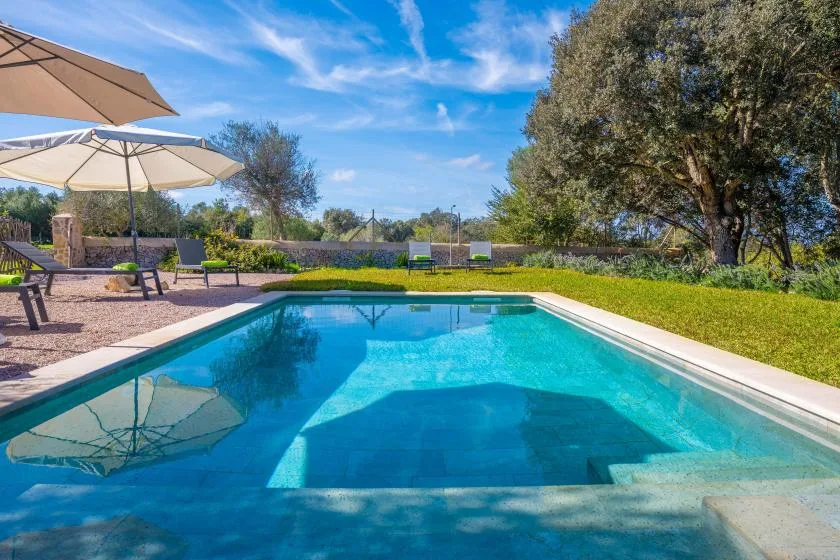Una piscina junto a un patio pavimentado con asientos y sombrillas.