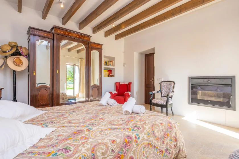 Dormitorio con una colcha estampada, armario de madera y vigas vistas en el techo.